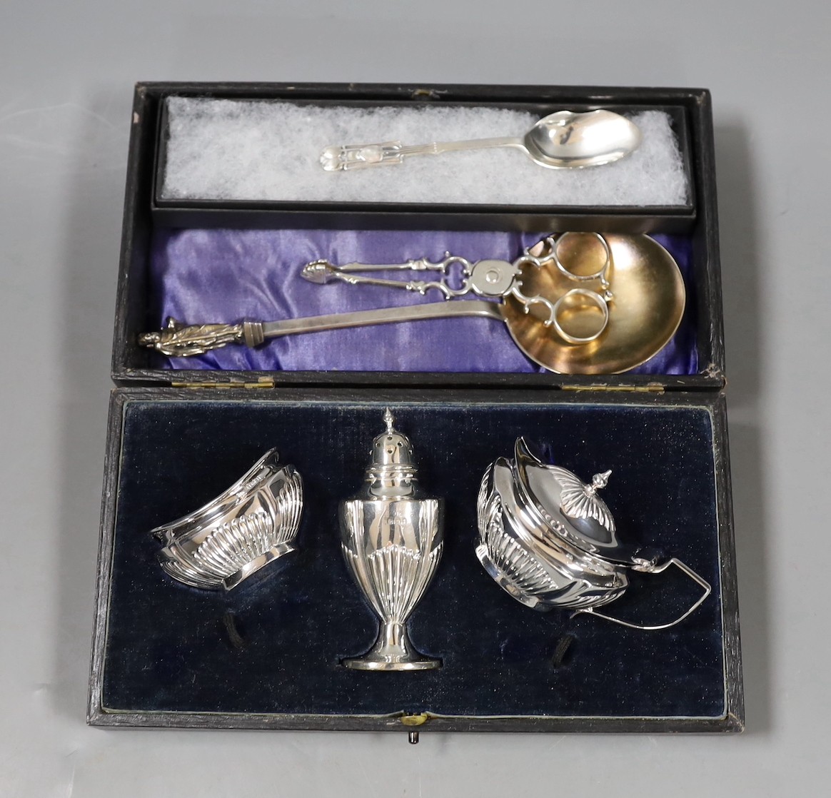 A cased George V silver three piece condiment set, lacking spoons, a 1930's Arts & Crafts sile r spoon by Liberty & Co, a Victorian silver apostle spoon and a pair of 18th century silver sugar nips.